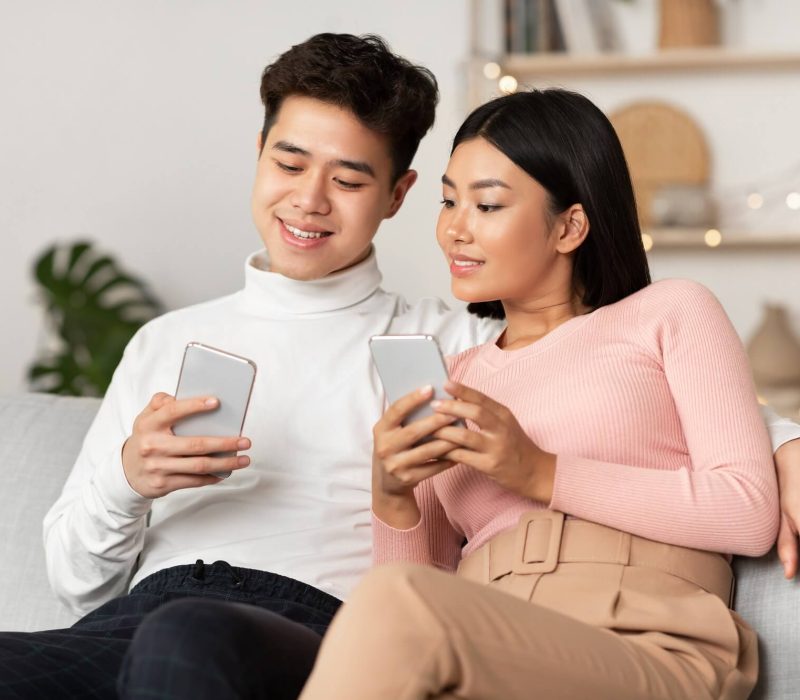 asian-couple-using-smartphone-phones-browsing-internet-sitting-at-home-1.jpg